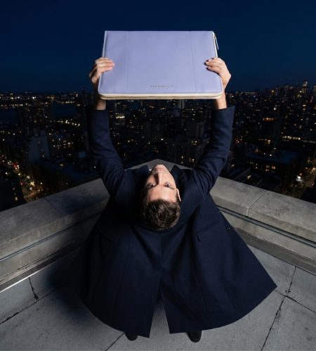 A model posing in a dynamic turn, holding the front of the STEFAN SERVAL Entrata Superiore luxury leather portfolio in pigeon blue with both hands.